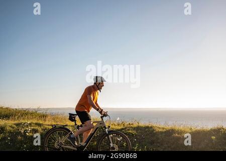 Sportif mature à vélo électrique par des plantes vertes Banque D'Images