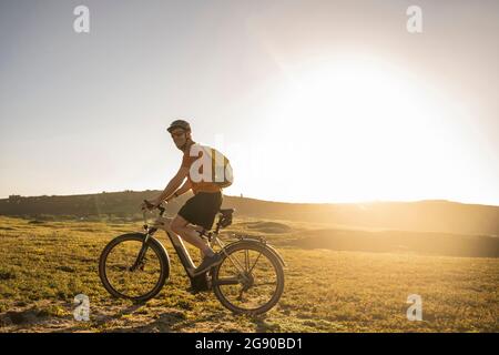 Sportif mature avec sac à dos à vélo électrique au coucher du soleil Banque D'Images