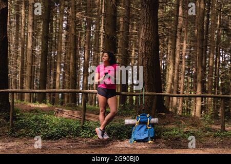 Une femme qui regarde loin tout en tenant son téléphone portable devant les arbres de la forêt Banque D'Images