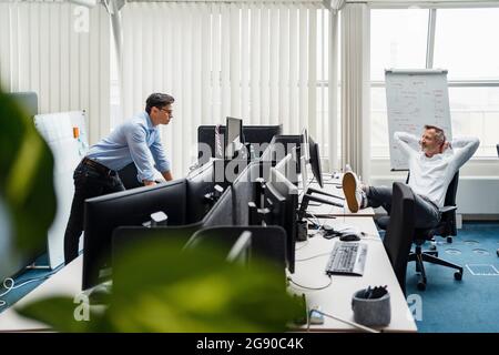 Homme d'affaires regardant un collègue reposant sur une chaise avec les mains derrière la tête dans le bureau Banque D'Images