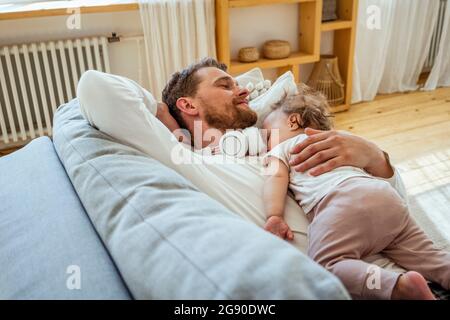 Homme avec fille dormant sur un canapé à la maison Banque D'Images