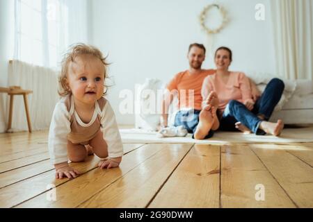 Jolie fille rampant tandis que la mère et le père assis sur le sol à la maison Banque D'Images