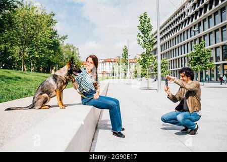 Homme photographiant une femme assise par un chien à travers un téléphone portable dans la ville Banque D'Images