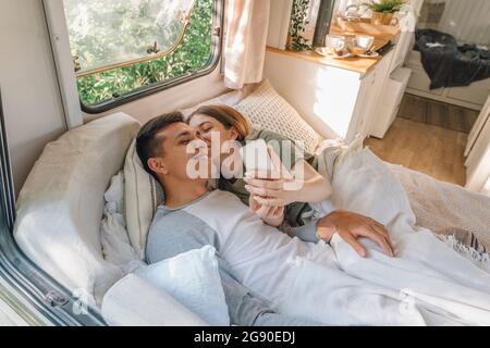 Femme embrassant un petit ami tout en prenant le selfie sur le lit dans la maison de moteur Banque D'Images