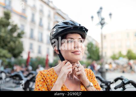 Femme souriante attachant un casque de cyclisme en ville Banque D'Images