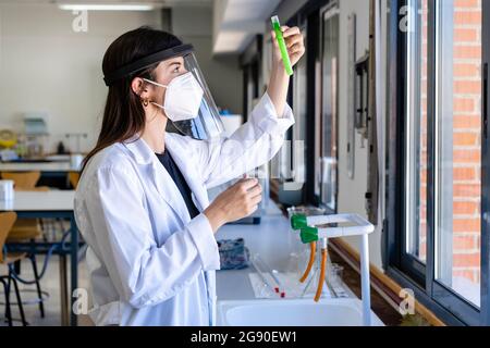 Jeune scientifique féminine portant un masque facial de protection examinant le produit chimique en laboratoire Banque D'Images