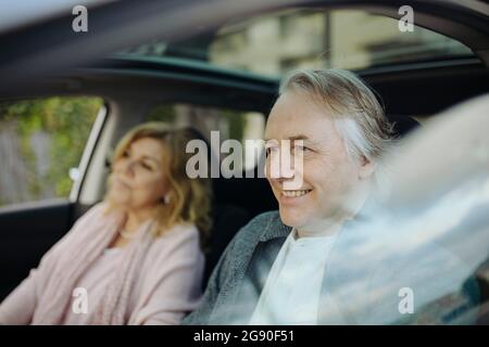 Homme mûr souriant assis avec une femme en voiture vu par une fenêtre en verre Banque D'Images