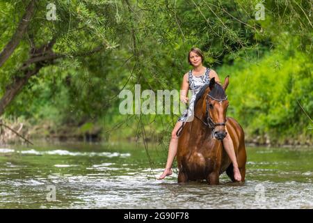 Jeune femme à cheval dans la rivière à la forêt Banque D'Images