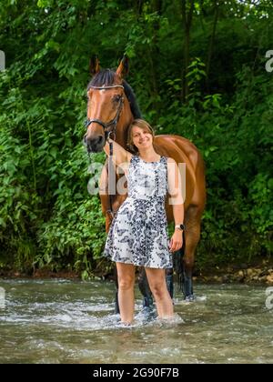 Femme souriante debout avec un cheval dans la rivière en forêt Banque D'Images
