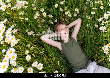 Garçon gai avec les mains derrière la tête reposant dans le champ de fleurs Banque D'Images