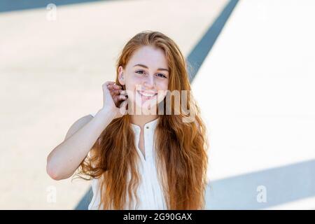 REDHEAD femme travailleur indépendant avec main dans les cheveux sur le banc pendant la journée ensoleillée Banque D'Images