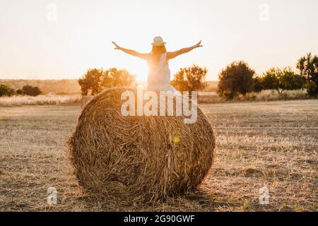 Femme insouciante avec bras étirés assis sur une balle de paille dans le champ Banque D'Images