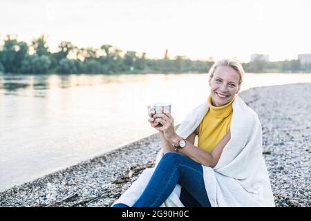 Femme souriant tout en tenant une tasse de café près de la rive Banque D'Images