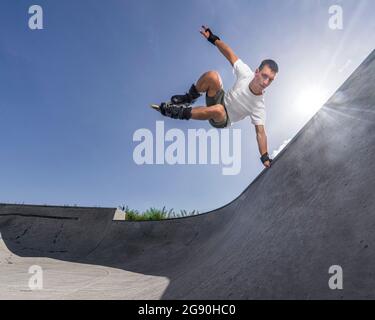 Homme faisant des cascades d'équilibrage dans les patins à roulettes le jour ensoleillé Banque D'Images