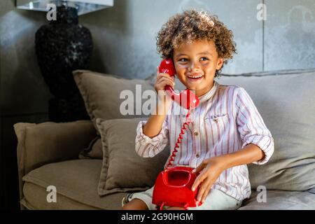 Afro garçon souriant tout en jouant avec le téléphone jouet sur le canapé Banque D'Images