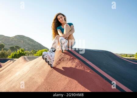 Jeune femme aux cheveux bruns portant des patins en ligne assis sur la piste de pompe Banque D'Images