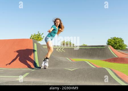 Jeune femme avec la main dans le patinage à roulettes de cheveux sur la piste de pompe pendant la journée ensoleillée Banque D'Images