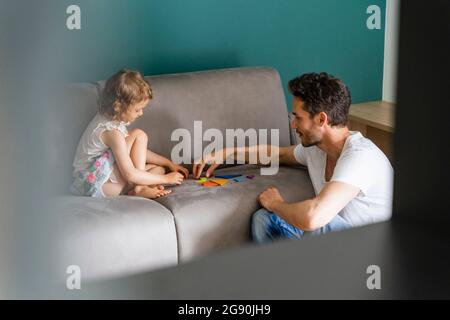 Père aidant la fille en jouant avec le puzzle sur le canapé Banque D'Images