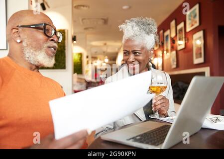 Femme d'affaires senior qui tient un verre tout en regardant un collègue de sexe masculin dans le restaurant Banque D'Images