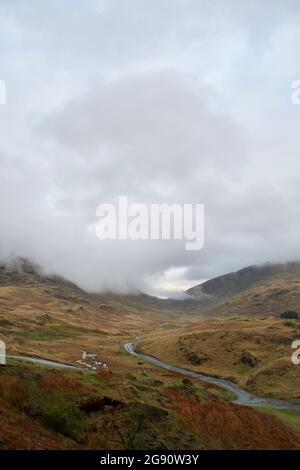 Une route de montagne (Pass) : route à voie unique qui s'enorne entre des landes herbeuses brunes, les sommets de montagne cachés dans le nuage bas et la brume. Couleurs d'automne en wi Banque D'Images