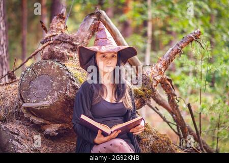 Une jeune sorcière se trouve dans les bois sur une souche avec un livre Banque D'Images