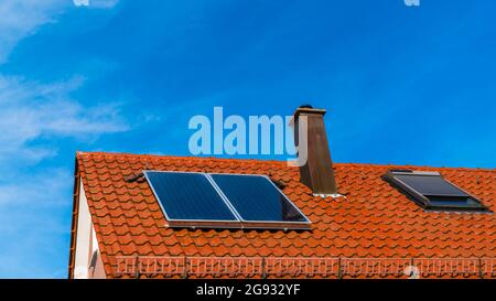 Panneaux solaires sur le toit rouge d'une maison générant de l'énergie propre pour l'eau chaude par la puissance de la lumière du soleil fournissant l'énergie pour le bâtiment Banque D'Images