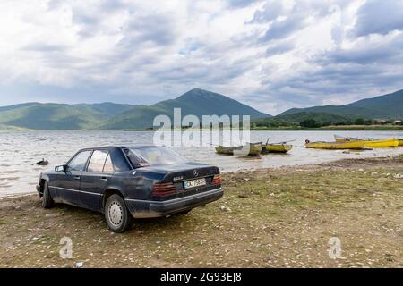 Vieille voiture Mercedes garée sur une rive du lac de Prespa à proximité des bateaux de pêche locaux, situé sur le tripoint de Macédoine du Nord, Albanie et Grèce Banque D'Images