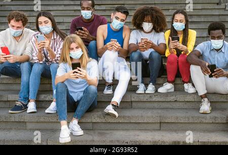Jeune groupe multiracial d'amis utilisant un smartphone mobile tout en portant un masque pendant le covid19 - concept de style de vie millénaire pour les jeunes Banque D'Images