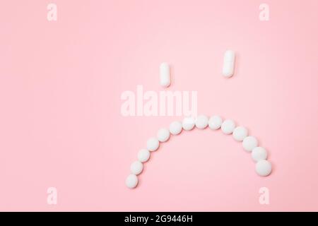 Préjudice pharmaceutique. Sad Smiley visage fait de pilules blanches, couché sur le Backgrond rose. Industrie pharmaceutique mondiale et médicaments Banque D'Images