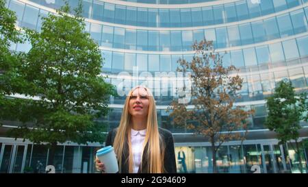 Par en dessous de la blonde woman in suit le café dans la tasse de papier à l'écart sur rue. Banque D'Images
