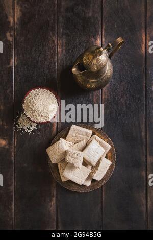 Morceaux de tahini halva, graines de sésame dans un bol, une carafe d'époque. Encore la vie dans le style oriental sur un vieux fond de bois brun, plat couché sur le dessus de la vue Banque D'Images