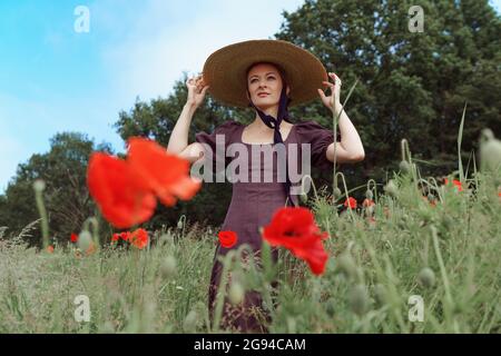 portrait de femme avec chapeau assis parmi les fleurs de coquelicots Banque D'Images