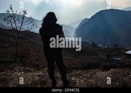 jeune fille regardant la vallée de montagne brumeuse avec des rayons du soleil le matin à partir d'un angle plat Banque D'Images