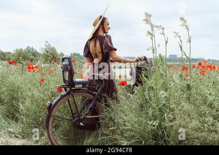 Femme avec vélo debout parmi les coquelicots champ contre le ciel Banque D'Images