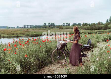 Femme avec vélo debout parmi les coquelicots champ contre le ciel Banque D'Images
