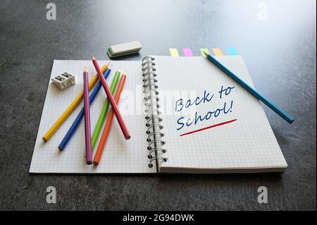 Cahier spirale avec texte Back to School, crayons de couleur, taille-crayon et gomme sur un bureau gris foncé, mise au point sélectionnée, profondeur de champ étroite Banque D'Images