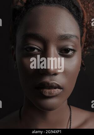 Portrait d'une jeune femme africaine confiante. Beau visage, peau brune, yeux et lèvres. La femme est sérieuse et calme. L'ombre se trouve sur un côté de la face. Photo verticale sur fond noir. Banque D'Images