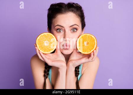Photo portrait de la jeune femme tenant deux oranges fraîches envoyant un baiser d'air isolé sur fond de couleur pourpre pastel Banque D'Images