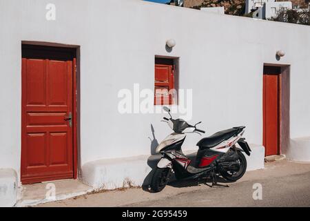 Agios Ioannis, Grèce - 24 septembre 2019: Moto garée par une maison typique blanchie à la chaux avec des portes et des fenêtres rouges sur l'île grecque de Mykonos, Banque D'Images