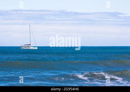 Image d'un bateau à voile qui est ancré près de la côte par un jour calme avec une mer calme et quelques nuages. Copier l'espace Banque D'Images