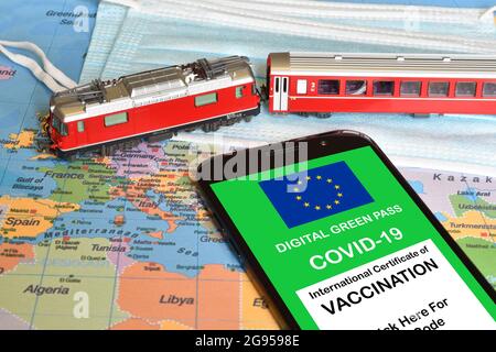 Le passe vert numérique de l'Union européenne sur smartphone avec un modèle de train rouge et surgìcal masque sur une carte géographique. Concept de voyage sécurisé duri Banque D'Images