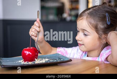 Petite fille mignonne à manger de la mousse au chocolat en forme de cerise, un dessert français avec une base de biscuits, du glaçage et des fruits. Banque D'Images