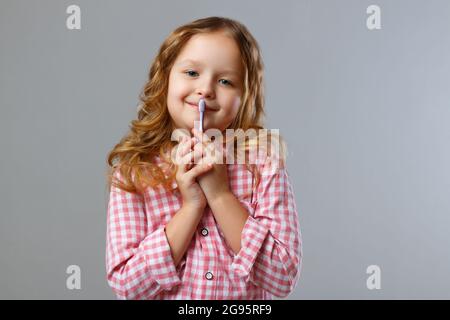 Petite fille tenant une brosse à dents. Enfant sur fond gris. Banque D'Images