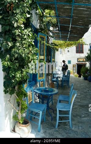 Une ruelle étroite avec des fleurs et des vignes au coeur de la vieille ville de la belle île grecque d'Amorgos. Tables et chaises dans une petite taverne. Banque D'Images