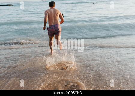 Un homme adulte court dans l'océan sur la plage de Waikiki Banque D'Images