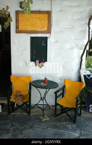 Une taverne à l'ancienne sur la belle île grecque d'Amorgos. Une petite table à l'entrée avec des chaises colorées. La vieille ville, la Hora sur une somme Banque D'Images