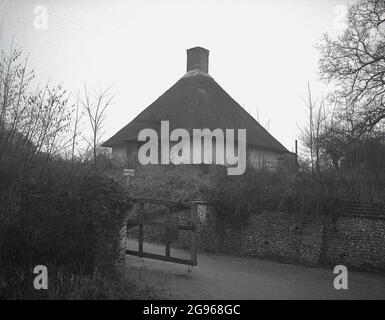 1950s, vue historique et extérieure d'un chalet rural sur South Downs, East Sussex, Angleterre, Royaume-Uni avec un toit de chaume en forme de cône inhabituel avec cheminée centrale. Banque D'Images