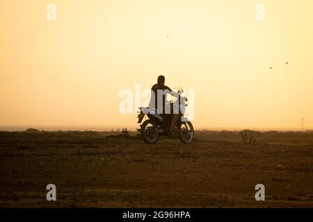 Uribia, la Guajira, Colombie - Mai 28 2021: L'homme latin de conduire une moto avec un fond jaune par les lumières du soleil de lever du soleil Banque D'Images