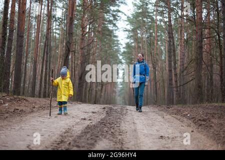 Maman et enfant marchent dans la route forestière après la pluie en imperméable ensemble Banque D'Images