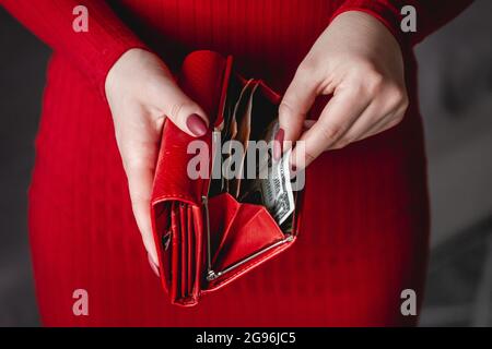 Portefeuille rouge entre les mains d'une femme dans une robe rouge avec manucure rouge Banque D'Images